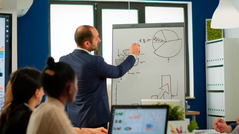professional-business-coache-company-leader-teacher-offering-flip-chart-presentation-explaining-graphs-consulting-with-clients-training-diverse-workers-group-conference-mee